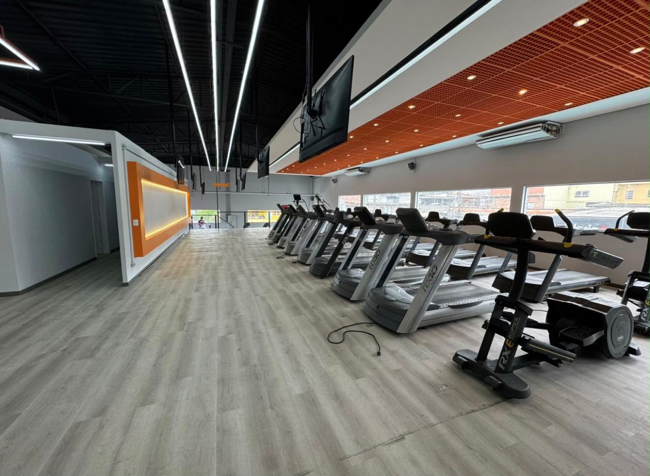 Área de cardio com forro metálico laranja e iluminação linear entregue pela RGK