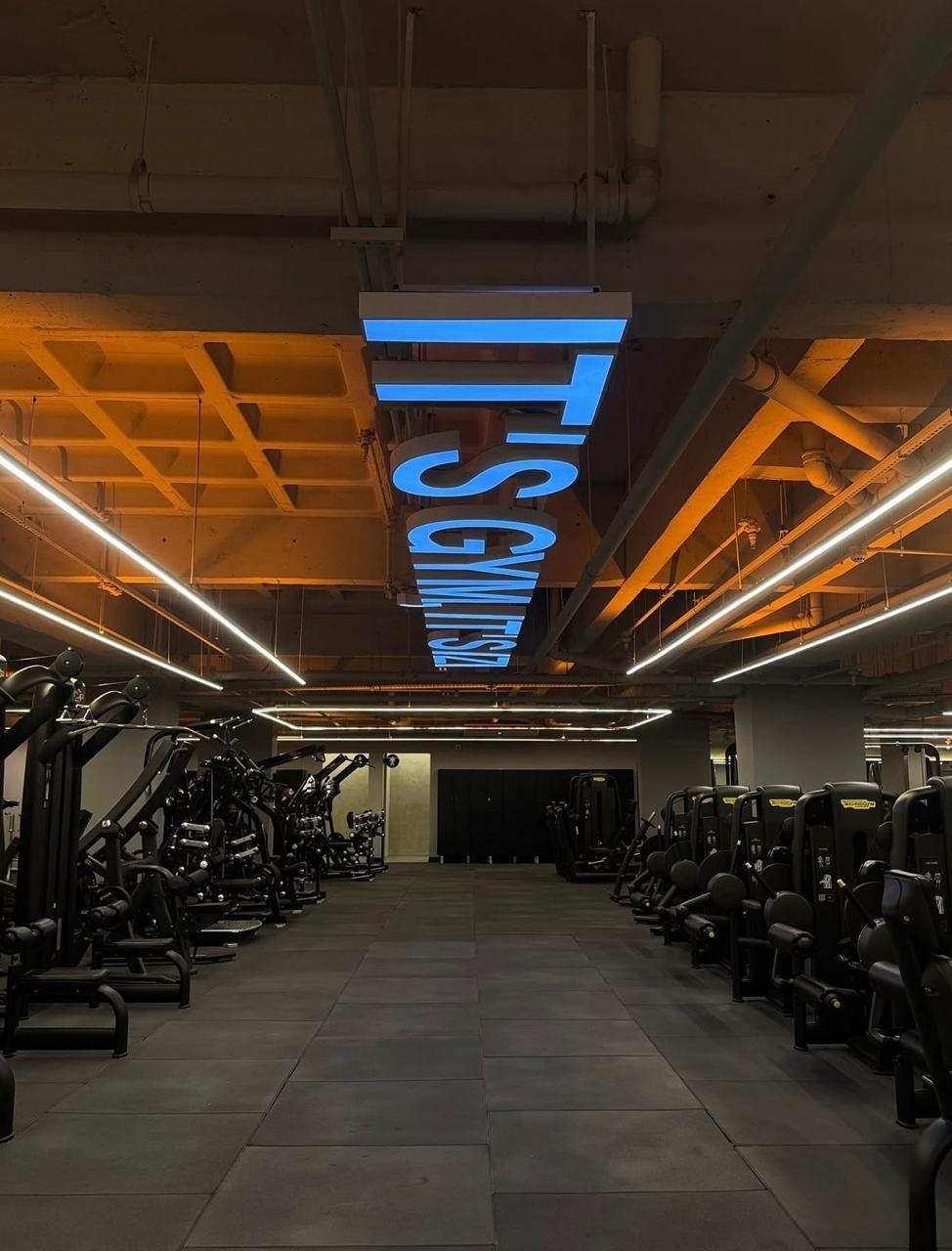 Salão de musculação com letreiro em neon azul e teto industrial aparente